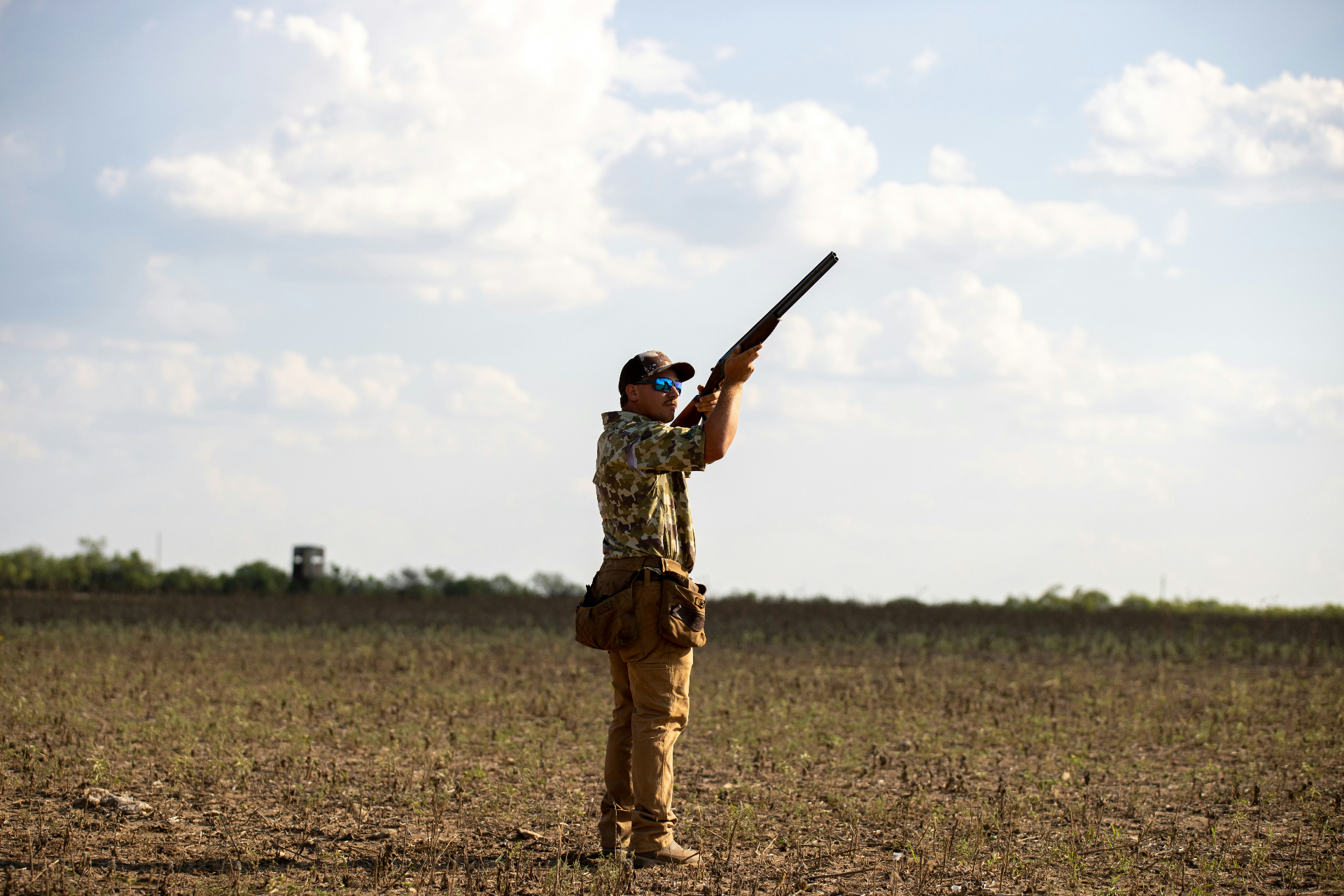 Hunter shouldering a shotgun in an open Arkansas field